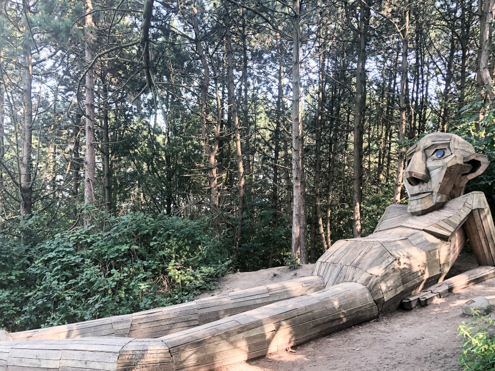 Uno de los trolls gigantes de madera, recostado en el bosque.