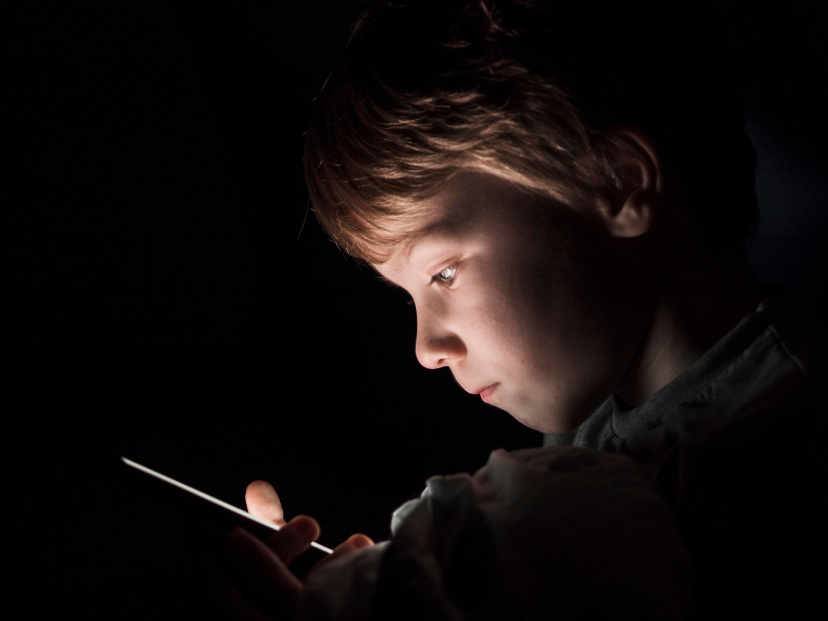 Imagen de Freepik. Niño rubio de unos 5 años mirando el teléfono en la oscuridad. Tema: lucha contra el grooming