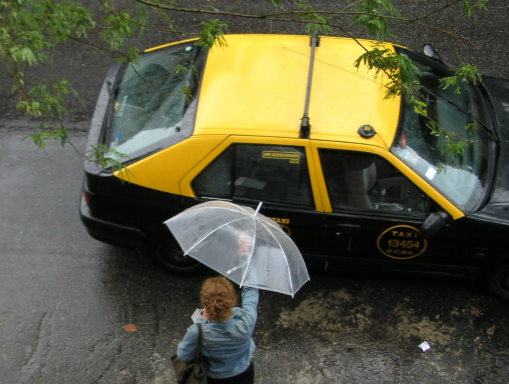 mujer subiendo a un taxi bajo la lluvia con un paraguas. tacho tachero