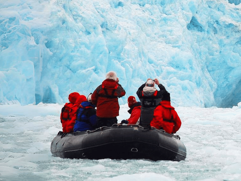 un grupo de personas con camperas rojas en una balsa frente a un glaciar haciendo ecoturismo