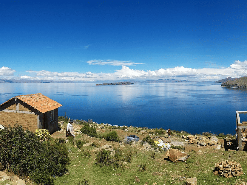 lago más grande de Bolivia. el titicaca. azul y una persona caminando por el pasto y una casita.