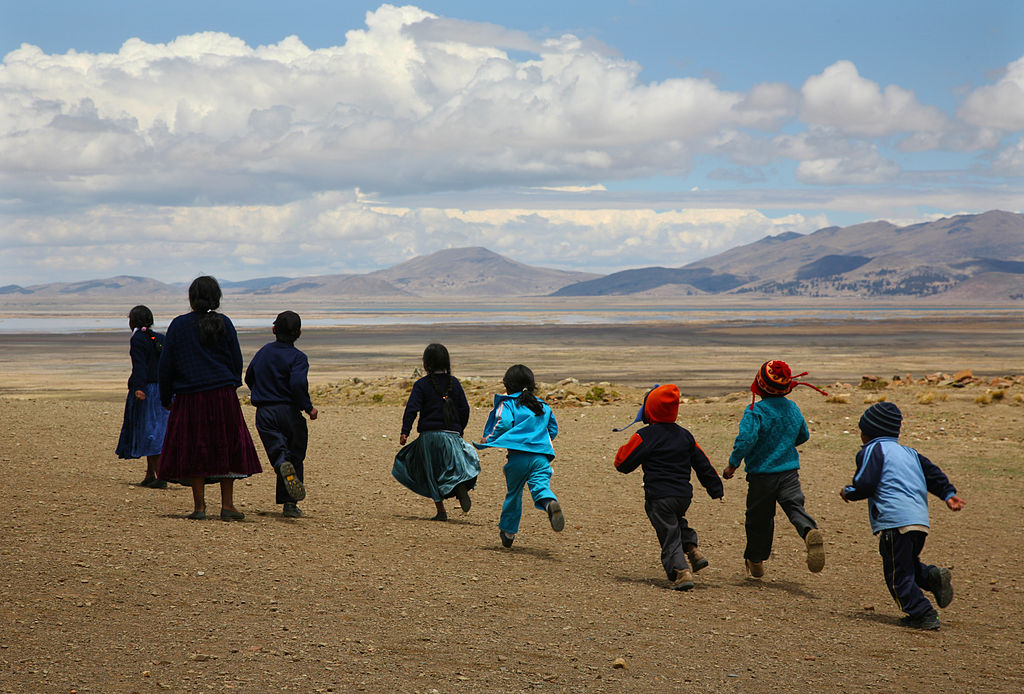 chicos bolivianos corriendo en la llanura con sus madres de espaldas