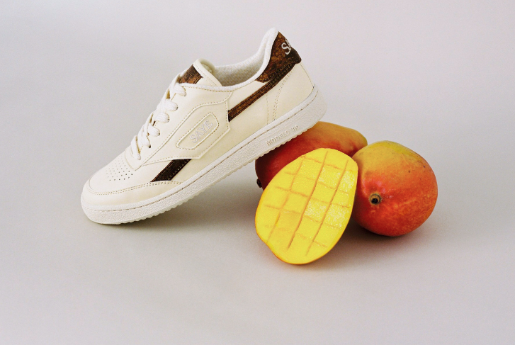 una zapatilla blanca y marrón sostenida sobre 3 mangos hecha de cuero de mango