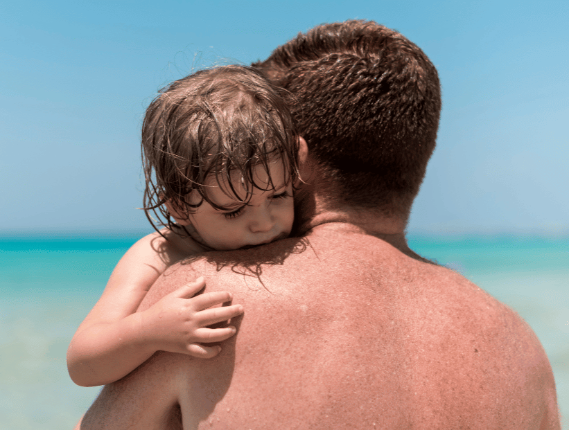 un señor hombre con un niño pequeño en sus brazos aplaudir en la playa