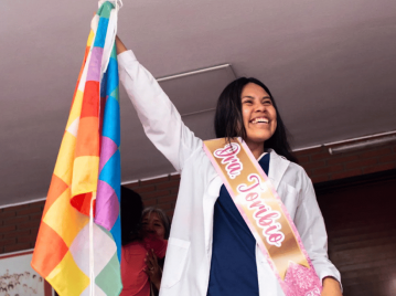 primera médica recibida wichi. mujer andina con ambo de médica sosteniendo la bandera de los pueblos originarios, sonriendo