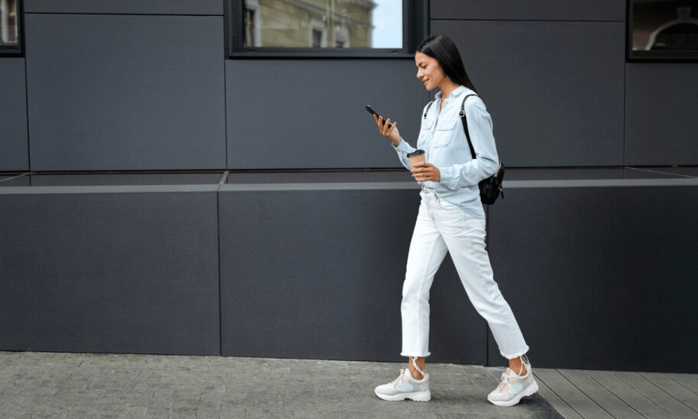 mujer de pelo negro caminando mientras mira el teléfono celular movil