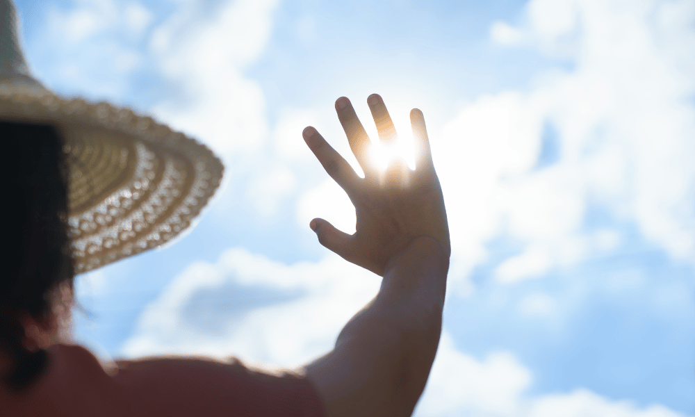 mujer con mano hacia el cielo y la luz del sol escapando por sus dedos. con sombrero de paja