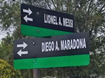 cartel que indica el cruce entre la calle messi y maradona en la provincia de la pampa con arboles atrás