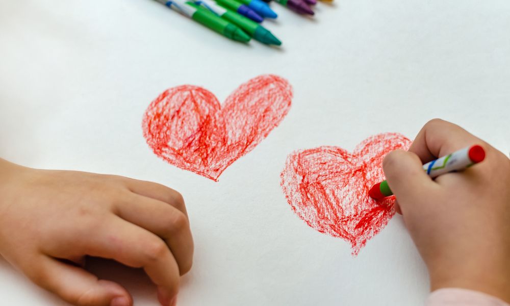 manos de infante dibujando corazones con crayones rojos