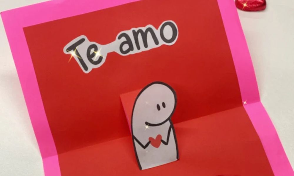 carta de san valentín roja y rosa con un tipito que sostiene un corazón y dice te amo