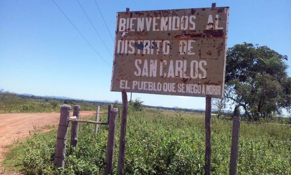 Cartel oxidado en un campo, que lee "bienvenidos al distrito de san carlos el pueblo que se negó a morir".