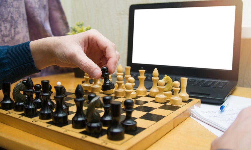 mano moviendo piezas de ajedrez en una tabla con una computadora en frente