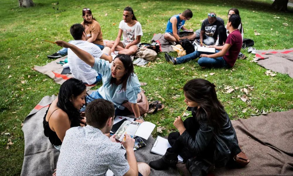 grupo de estudiantes reunidos en un parque hablando en rondas con mantas sobre el pasto césped