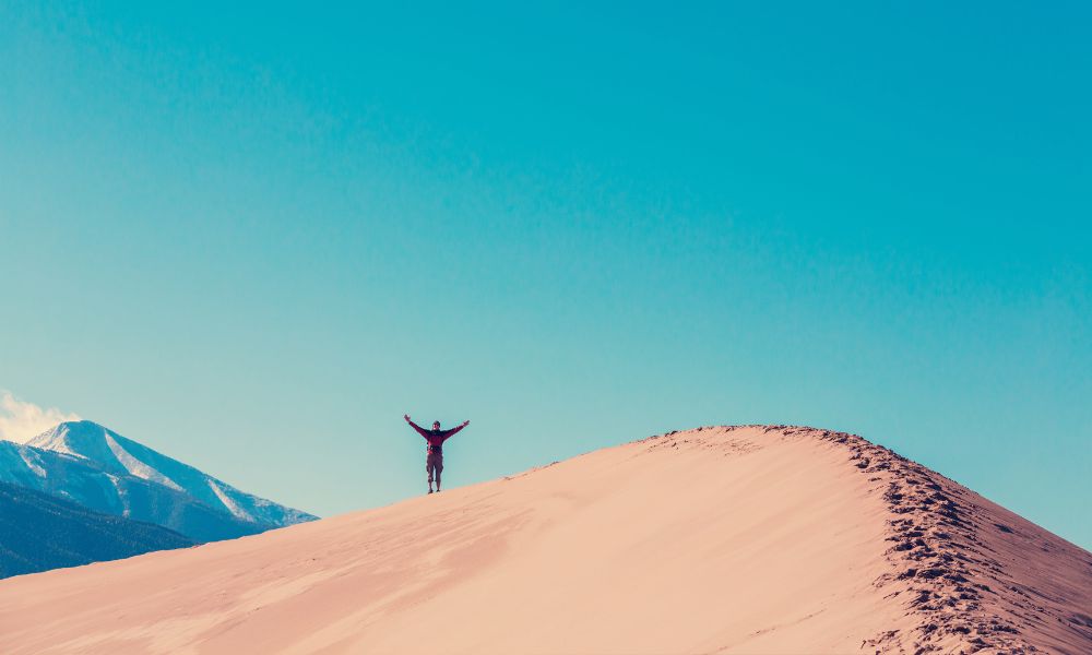 un hombre levantando los brazos en la cima de una duna de arena