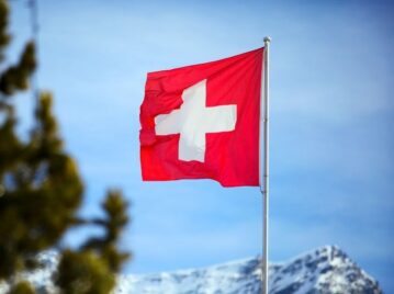 bandera de suiza flameando al lado de un pino con el cielo azul