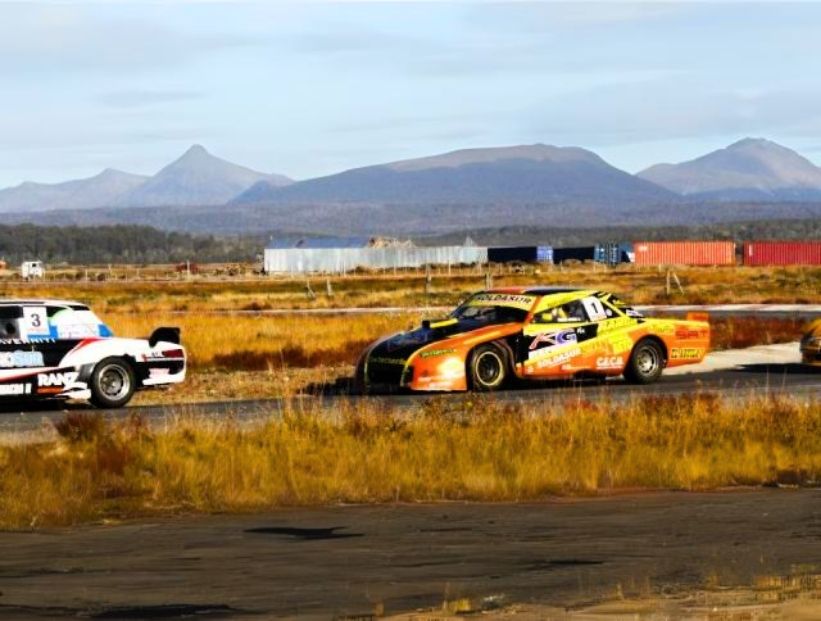 autódromo más al sur del mundo tres autos de carreras en un circuito con pastizales amarillos y marrones y montañas de fondo