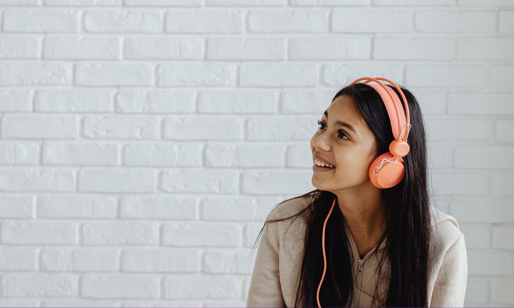 una adolescente escuchando música con auriculares naranjas