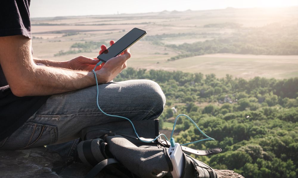 hombre sentado en monte usando el teléfono mientras carga