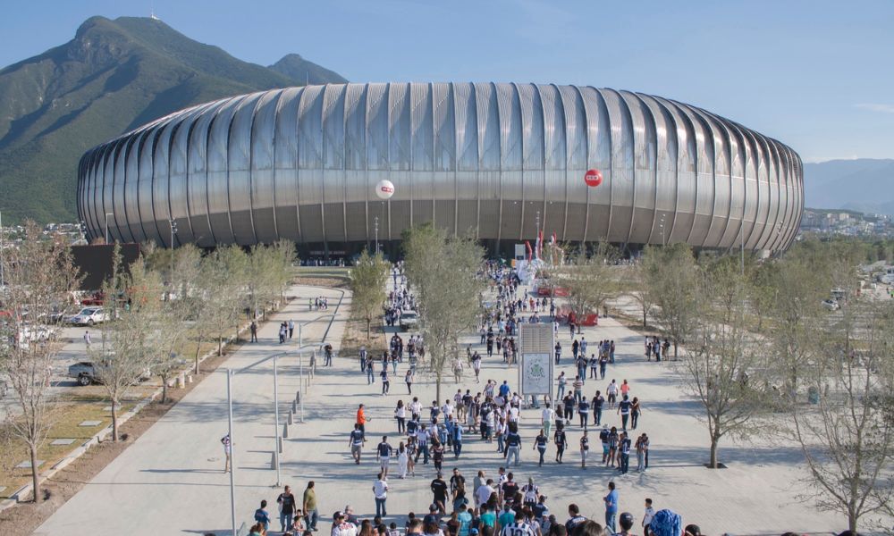 personas entrando a un estadio gris con montañas de fondo